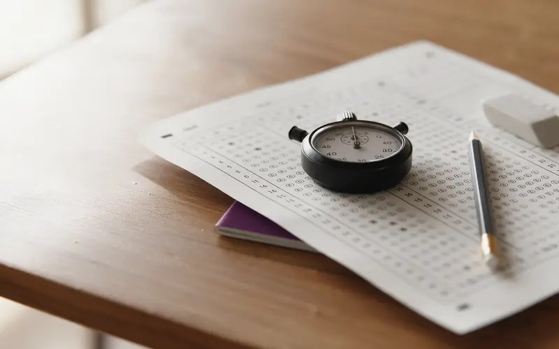 A multiple-choice answer sheet with a stopwatch, pencil and eraser on a study desk
